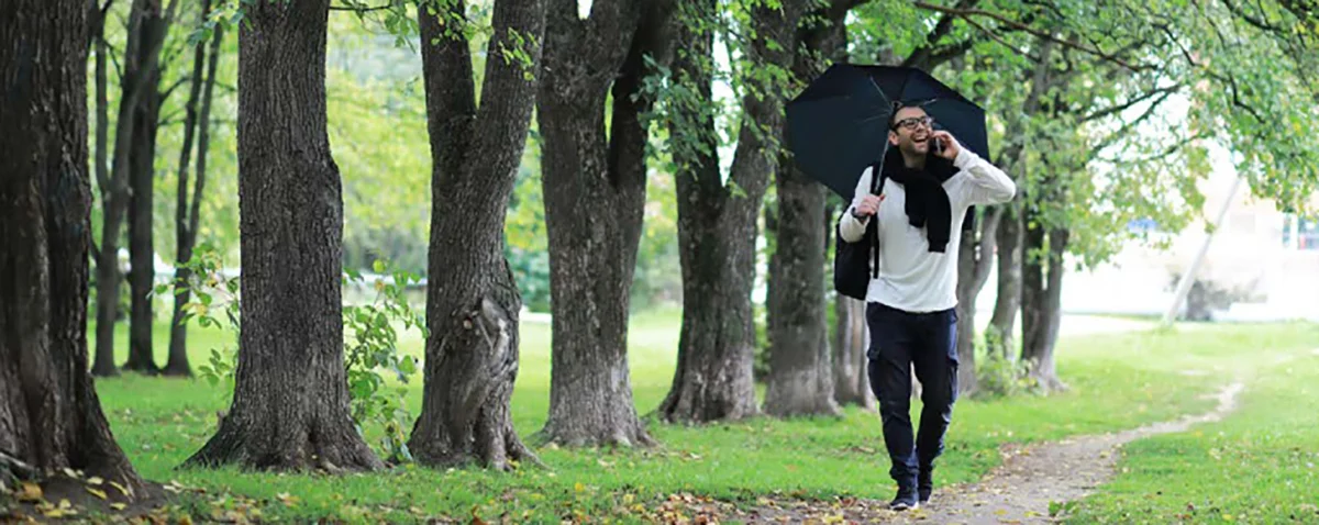 Man walking in the park talking on cell phone with umbrella