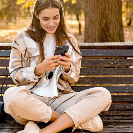 Lady sat on a park bench shopping on her phone.