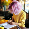 a person with pink hair writing on a book