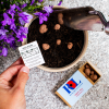 a hand holding a small piece of paper next to a potted plant