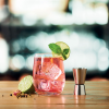 a glass of red liquid with ice and a slice of lime on a wooden surface