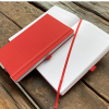 a red and white notebooks on a wooden surface