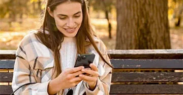 Lady sat on a park bench shopping on her phone.